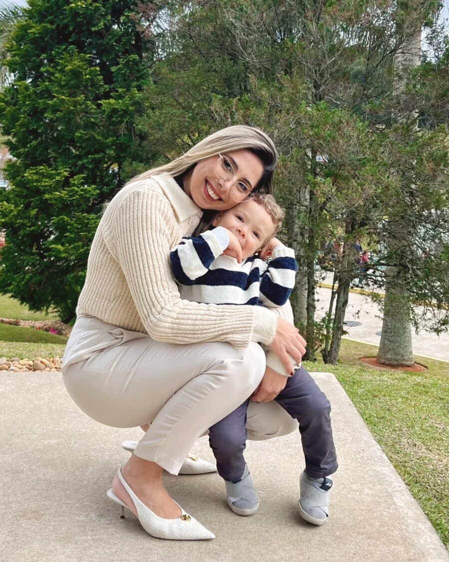 Pâmela Pissutti agachada, abraçando seu filho ao ar livre